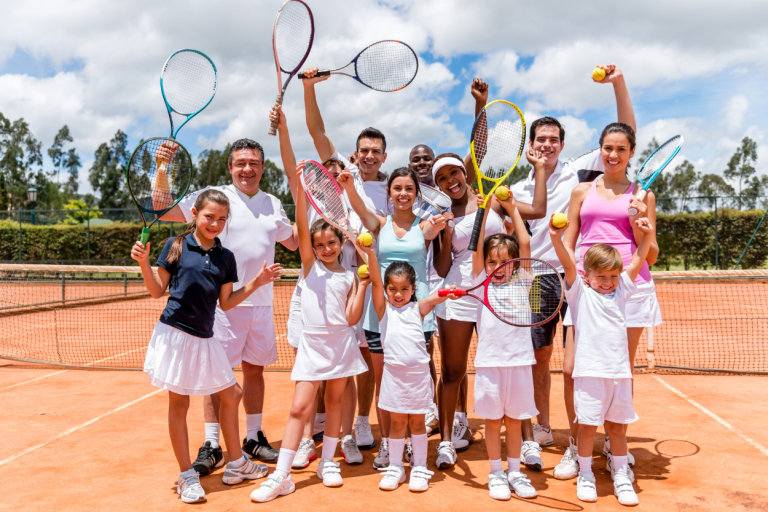 Kinder und Erwachsene mit Tennisschlägern Eine Gruppe von Tennis-Spielern in weißen Outfits posiert fröhlich auf dem Tennisplatz.